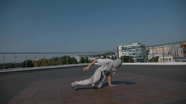 The guy coolly dances breakdance on the roof of the house. A man dances an energetic athletic dance.	
