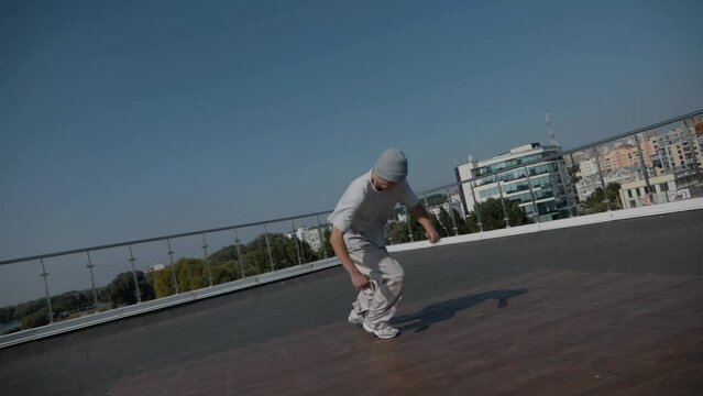 The guy coolly dances breakdance on the roof of the house. A man dances an energetic athletic dance.