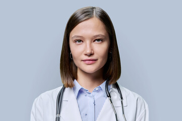 Headshot portrait of young friendly female medical worker on gray background
