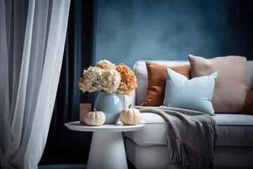Gardinen A vase with dry hydrangea and pumpkins on the table by the sofa. Autumn living room interior in blue and orange tones. © July P