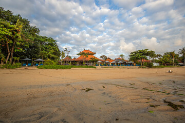 Fototapeta na wymiar Magical sunrise with clouds in the sky. Dramatic sky at Sanur beach, Denpasar in Bali. Temple in the calm sea in the morning. Tropical landscape shot