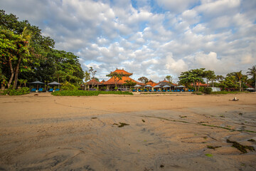 Magical sunrise with clouds in the sky. Dramatic sky at Sanur beach, Denpasar in Bali. Temple in the calm sea in the morning. Tropical landscape shot