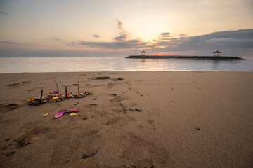 Fototapeta na wymiar Sunrise at the sandy beach of Sanur. Temple in the water. Offerings by the sea on the beach. Hindu faith in Sanur on Bali. Dream island and dream destination