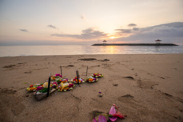Sunrise at the sandy beach of Sanur. Temple in the water. Offerings by the sea on the beach. Hindu...