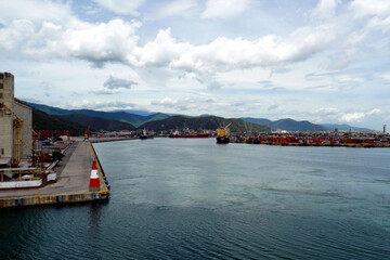 Port basin of Puerto Cabello with moored ships in container and general cargo terminal. In the corner is small red and white lighthouse. There is green mountain.
