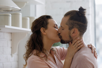 Relaxed sincere young couple kissing in kitchen, hugging with love, tenderness, passion, enjoying closeness, dating, living together, leisure time at home. Relationship, romance concept