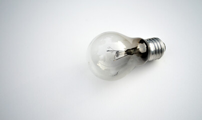 A glass burnt-out incandescent lamp on a white table.An old lighting lamp with a burnt-out spiral.