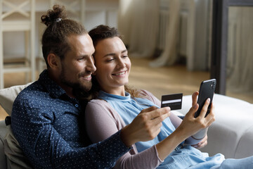 Young married couple of happy customers using smartphone and credit card for online payments from...