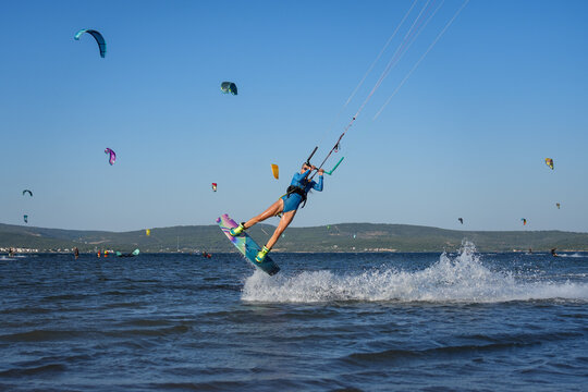 Beautiful girl  with blond hair kitesurfing in blue sea making jump tricks  with kites in the background