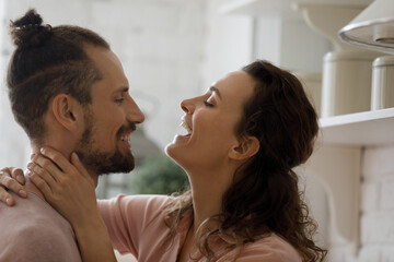 Cheerful excited young dating couple hugging with love, joy, enjoying romantic leisure time together at home. Boyfriend and girlfriend talking, laughing in kitchen domestic interior