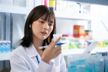 Female pharmacist hold pill in hand at drugstore. She checking drug detail at pharmacy shop.