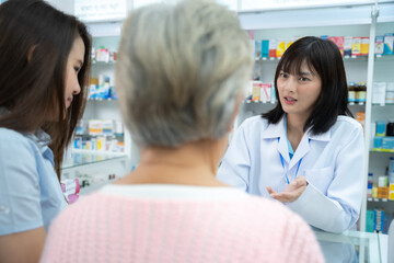 Obraz premium Young Asian pharmacist talking with customer at pharmacy counter. She tells customers about drug information at the pharmacy.