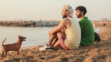 Beautiful gay couple in love talking and laughing while sitting on the beach at dawn, playing with...