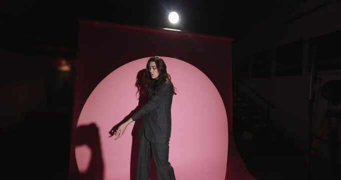 Backstage professional fashion photo shoot. Slow motion. Beautiful dark-haired girl model poses for photographer in light of white cyclorama on podium. Beautiful woman posing on pink background