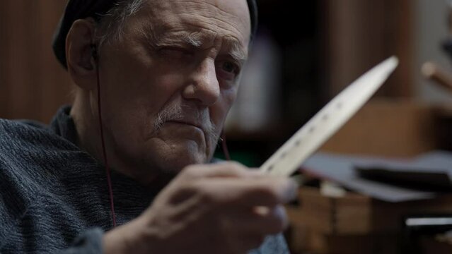 Senior gray haired male master in a wheelchair working at his workshop sharpening Japanese kitchen knife