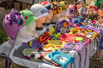 Knitted children's hats with animal faces are sold at a street stall. Handmade