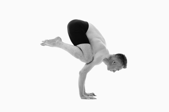Bakasana ( Crane pose), Ashtanga yoga  Side view of man wearing sportswear doing Yoga exercise against white background. Black and white image.