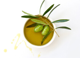 Extra Virgin Olive Oil in a white plate and with a branch of olives on a white background with drops of olive oil. Best taste of Greece, healthy organic food.