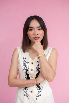 A typical asian woman with medium length hair wearing a cream sleeveless blouse. Against a pink background.