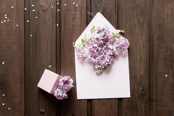 Square postage envelope and small gift box on wooden background, bouquet of lilac. Flat lay, top view. Happy mother's day, women's day or birthday, wedding composition. Blank greeting card, mockup