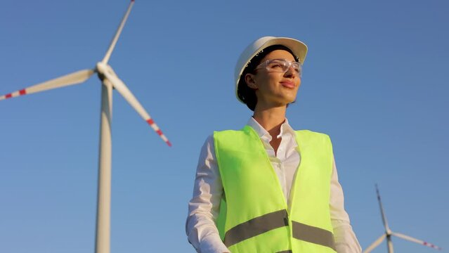 Portrait of woman engineer standing with hardhat and vest by the windmill turbines