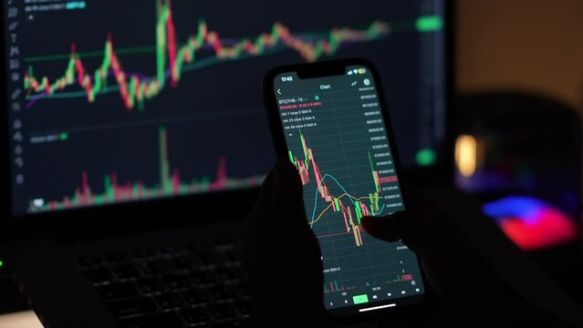 Investors trade cryptocurrencies using smartphone apps, analyzing financial data and stock market prices on mobile phones. Review the online trading platform application Buy cryptocurrency