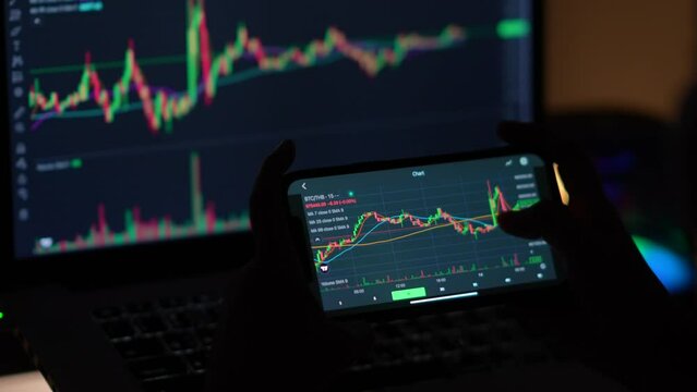 Investors trade cryptocurrencies using smartphone apps, analyzing financial data and stock market prices on mobile phones. Review the online trading platform application Buy cryptocurrency