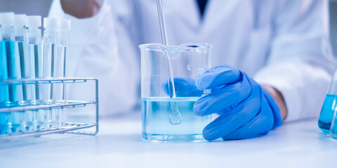 Closeup scientist hand using stirring rod for stirring blue liquid solution glass beaker chemical...