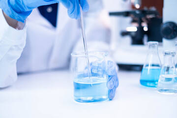 Closeup scientist hand using stirring rod for stirring blue liquid solution glass beaker chemical chemistry research science experiment test laboratory, scientific medicine technology lab analysis