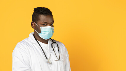 African American man doctor in protective face mask, yellow background