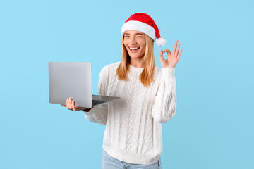 Xmas shopping online. Happy european lady in Santa hat holding laptop computer and showing ok sign, blue background