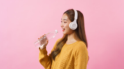 Young woman holding water bottle as microphone to singing a song isolated on pink background