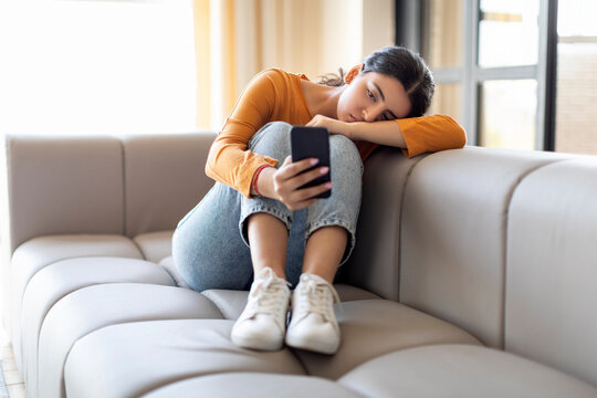 Boring Content. Bored indian woman with smartphone sitting on couch at home