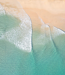 Portait view of an aerial shot over a beach with gentle waves slowly crashing on white sand