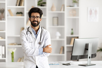 Indian Doctor Poses Beside Computer in Clinic Setting - obrazy, fototapety, plakaty