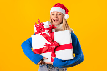 Excited european woman in sweater and Santa hat holding pile of gifts, celebrating winter holidays