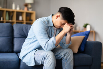 Korean guy crying resting head on fists sitting at home