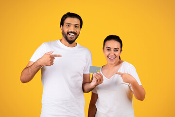 Cheerful millennial arab couple point finger at credit card, recommends sale, profit and savings