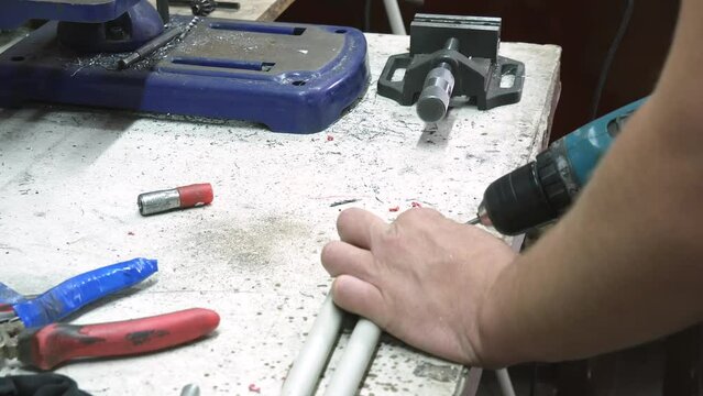 On a table in a workshop, a man prepares a plastic extension cord. He drills a hole to rivet the threaded adapter all the way to the rod. High quality 4k footage