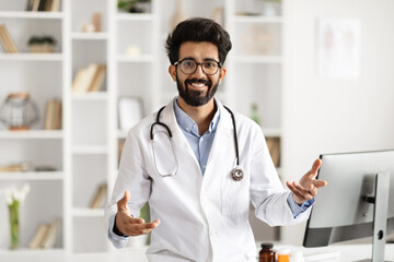 Portrait of cheerful eastern man doctor gesturing at clinic - obrazy, fototapety, plakaty