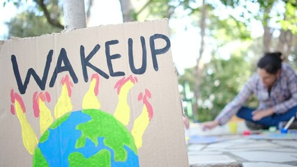 A mother and her two children prepare colorful protest signs against climate change and pollution using paintbrushes