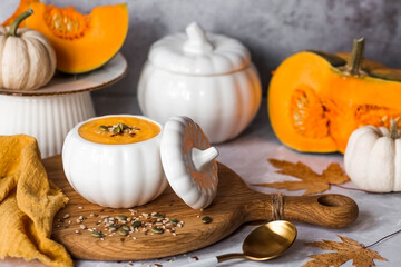 Seasonal autumn food. Traditional pumpkin cream soup in a pumpkin-shaped bowl and fresh pumpkin on a gray marble background.