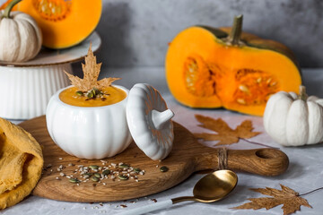 Seasonal autumn food. Traditional pumpkin cream soup in a pumpkin-shaped bowl and fresh pumpkin on a gray marble background.