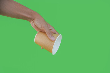 hand holding a Takeaway paper coffee cup. coffee to go in a disposable cup on a green background, you can place text or logo, kraft paper cup.