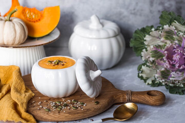 Seasonal autumn food. Traditional pumpkin cream soup in a pumpkin-shaped bowl and fresh pumpkin on a gray marble background.