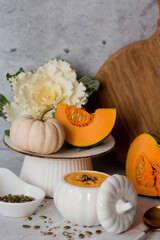 Seasonal autumn food. Traditional pumpkin cream soup in a pumpkin-shaped bowl and fresh pumpkin on a gray marble background.