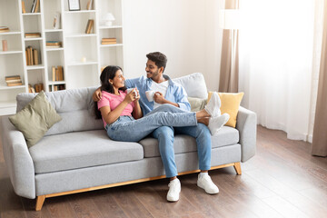 Smiling young indian couple drinking coffee and chatting on couch