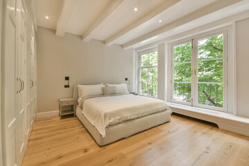 a bedroom with hardwood flooring and large windows looking out onto the trees in the distance is an empty bed