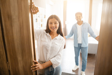 Indian couple warmly welcoming guests near the open door - obrazy, fototapety, plakaty