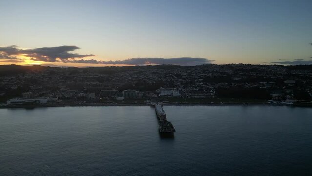 Paignton, Torbay, South Devon, England: DRONE VIEWS: Paignton Pier at sunset. Paignton is a popular UK holiday resort; the Pier was completed in 1879 during the reign of Queen Victoria (Clip 5).